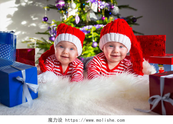 双胞胎开心微笑着身穿圣诞老人的帽子和衣服的趴着的婴儿微笑的小孩婴儿微笑